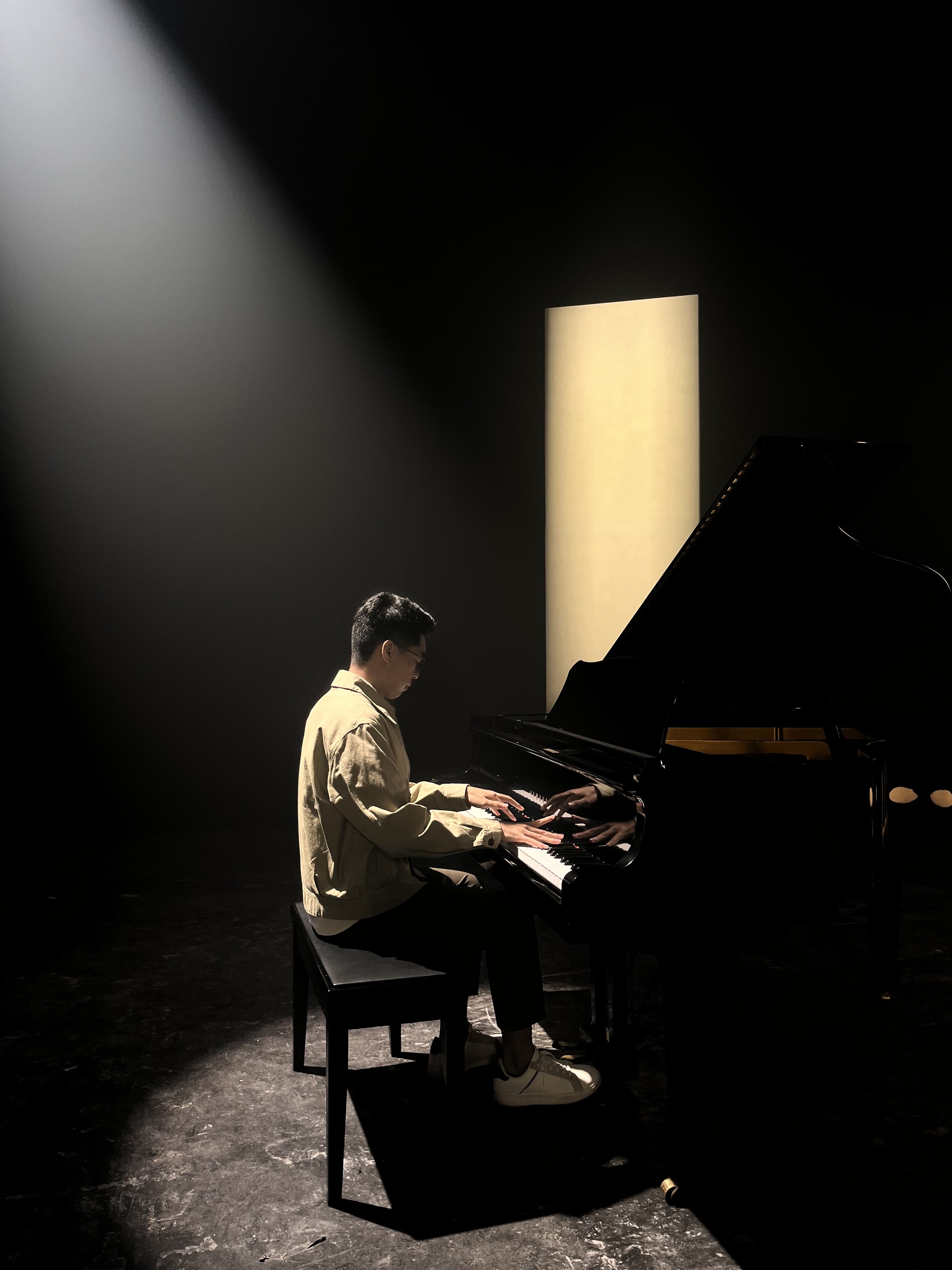 Jason Timothy Jopy at a grand piano under a single shaft of stage light